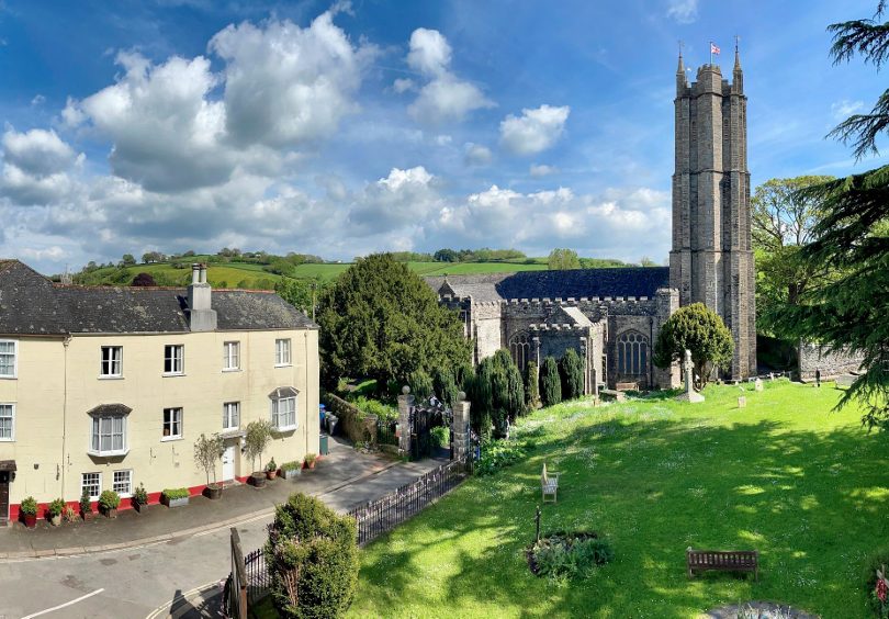 Church and house in Ashburton with grass churchyard in the foreground and a blue sky with a few clouds